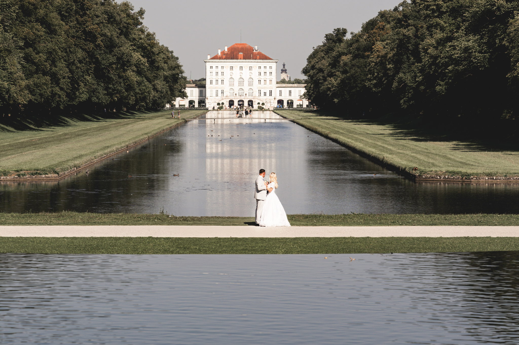 Bride and groom by the canal in front of Nymphenburg Palace in late afternoon light